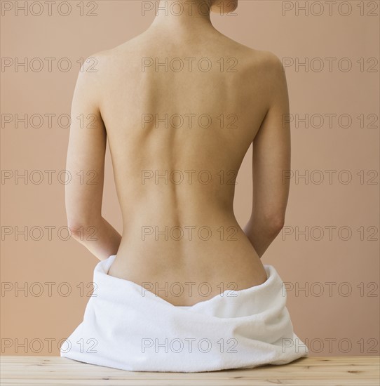 Rear view of nude woman with towel around hips.