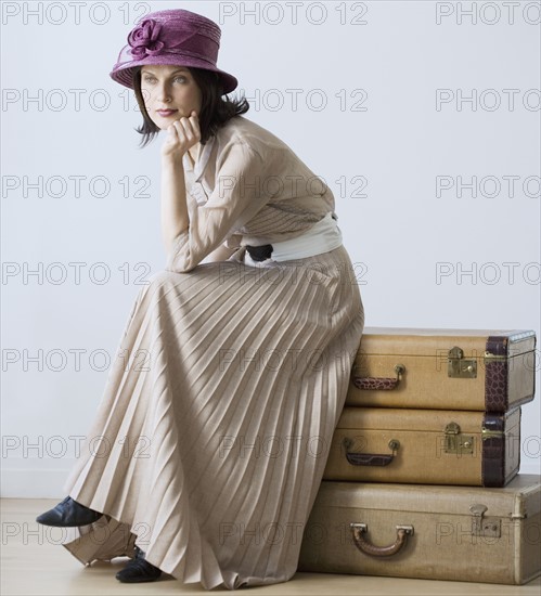 Woman in vintage clothing sitting on suitcases.