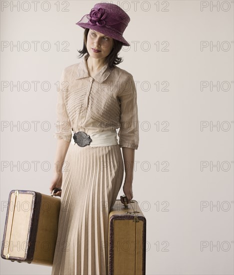 Woman in vintage clothing carrying suitcases.