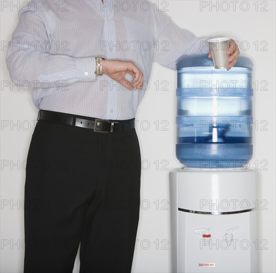 Businessman checking watch next to water cooler.