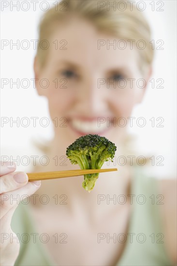 Woman holding broccoli in chopsticks.