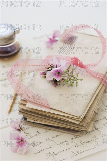 Stack of old letters next to flowers and ink bottle.