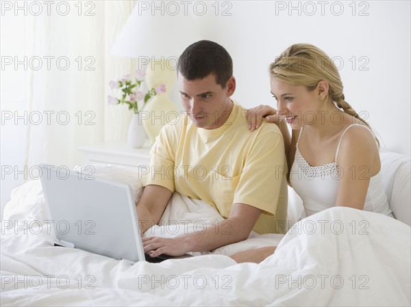 Couple looking at laptop in bed.