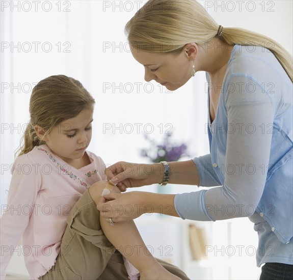 Mother bandaging daughter’s knee.