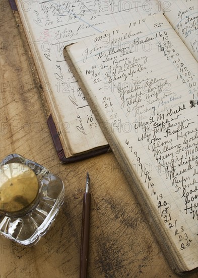 Quill pen and ink jar next to old ledger books.