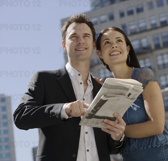 Couple holding newspaper in urban scene.