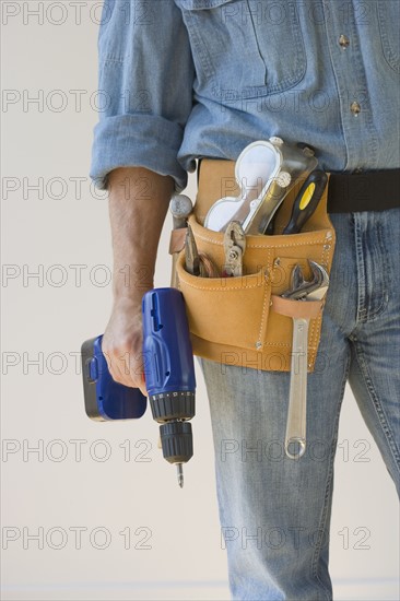 Man wearing tool belt and holding drill.