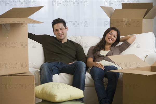 Multi-ethnic couple surrounded by moving boxes.