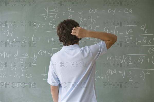 Teenaged boy looking at math equations on blackboard.