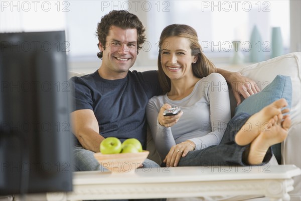 Couple watching television on sofa.
