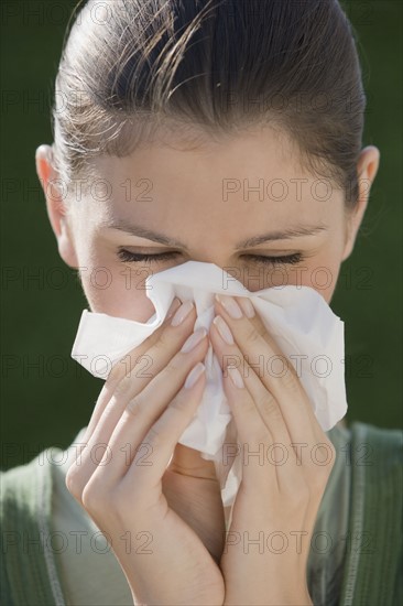 Young woman blowing nose.