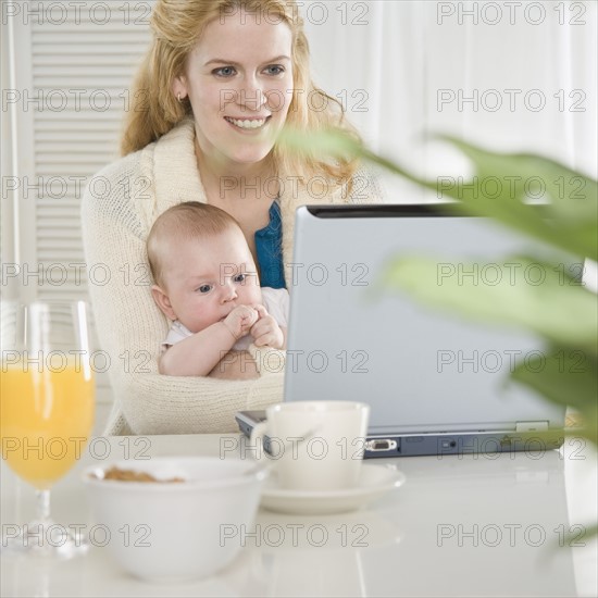 Mother holding baby and using laptop. Date : 2006
