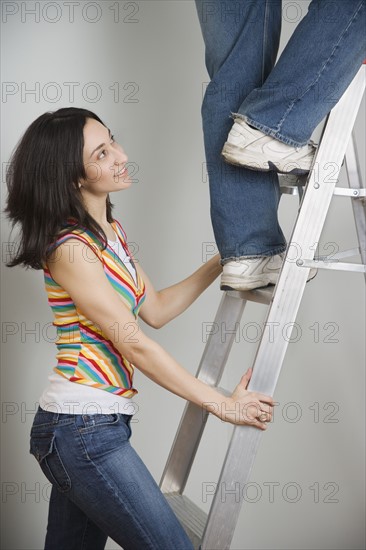Woman holding ladder while man climbs. Date : 2006