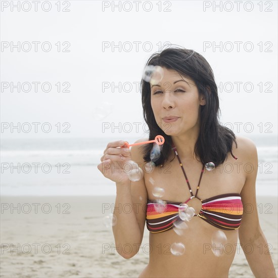 Woman in bikini blowing bubbles at beach. Date : 2006