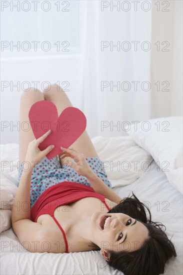 Woman holding paper cut out heart in bed. Date : 2007