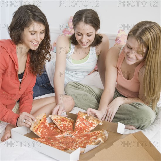 Teenage girls eating pizza on bed. Date : 2007