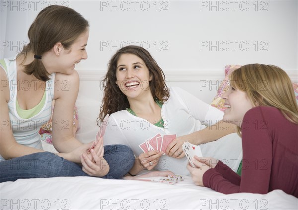 Teenage girls playing cards on bed. Date : 2007