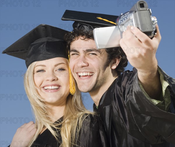 Couple in graduation caps and gowns video recording selves. Date : 2007