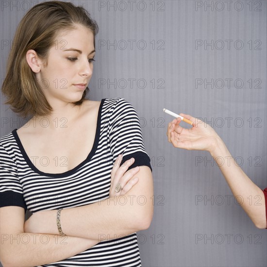 Teenage girl looking at cigarette in friend’s hand. Date : 2007