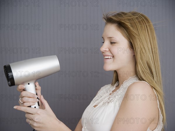 Teenage girl pointing hair dryer at face. Date : 2007