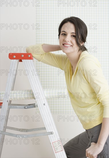 Woman on ladder with roll of wallpaper. Date : 2007