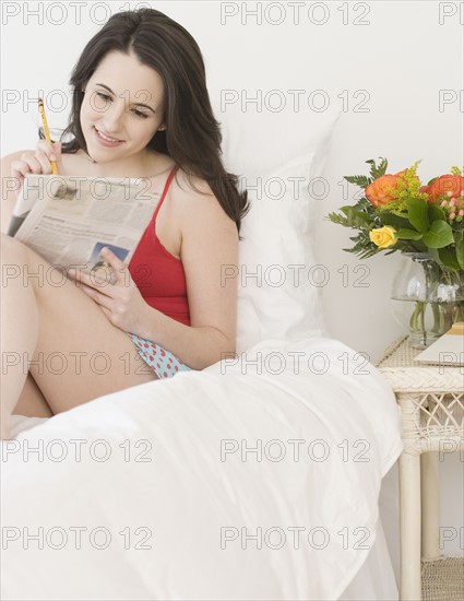 Woman reading newspaper in bed. Date : 2007