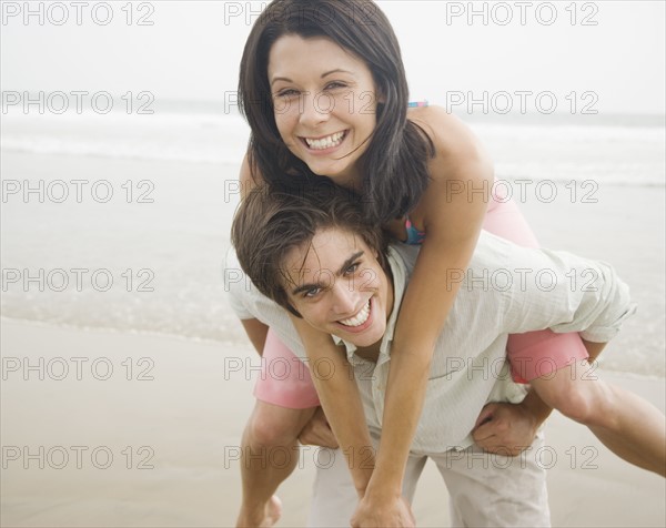 Man giving woman piggyback ride at beach. Date : 2006