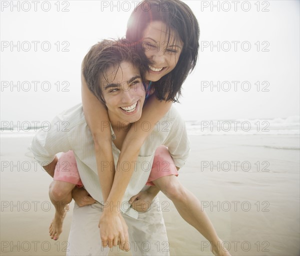 Man giving woman piggyback ride at beach. Date : 2006