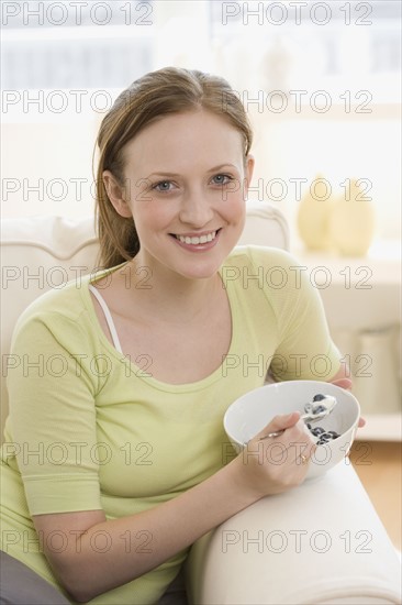 Woman eating bowl of fruit on sofa. Date : 2006