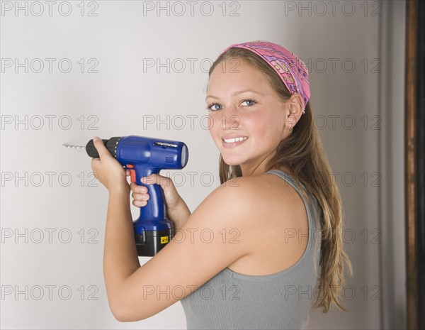 Young woman using cordless drill on wall. Date : 2006