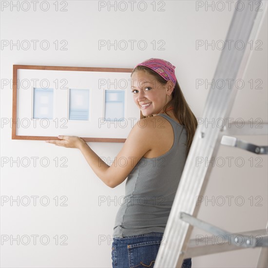 Young woman hanging picture on wall. Date : 2006