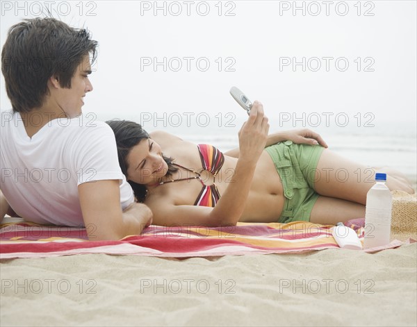 Couple with cell phone on blanket at beach. Date : 2006