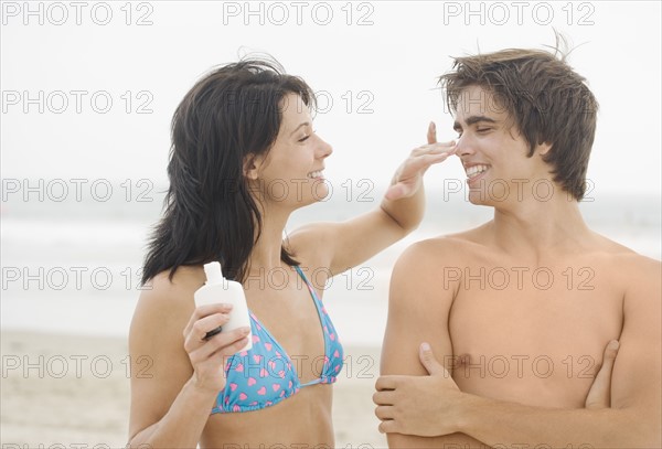 Woman putting sunscreen on man's nose at beach. Date : 2006