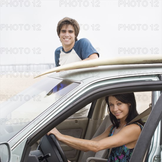 Couple and car with surfboard on top at beach. Date : 2006