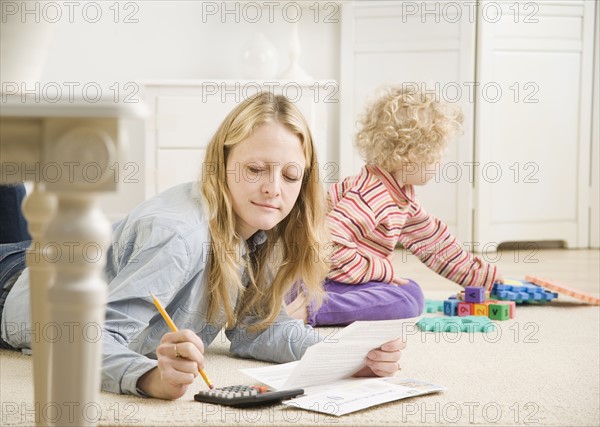 Mother working on calculator while child plays. Date : 2006