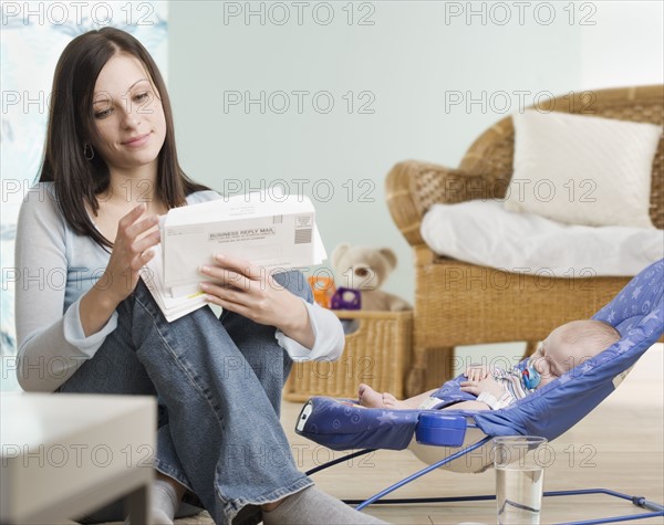 Mother looking at mail with sleeping baby. Date : 2006