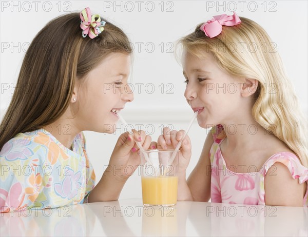 Young sisters sharing glass of juice with two straws. Date : 2006
