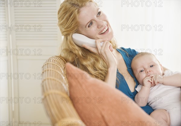 Mother holding baby and talking on the phone. Date : 2006