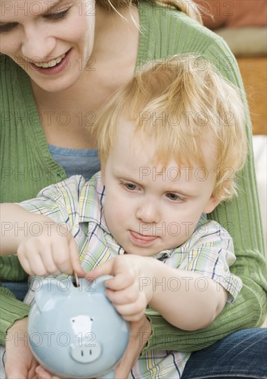Mother and young son putting change in piggy bank. Date : 2006