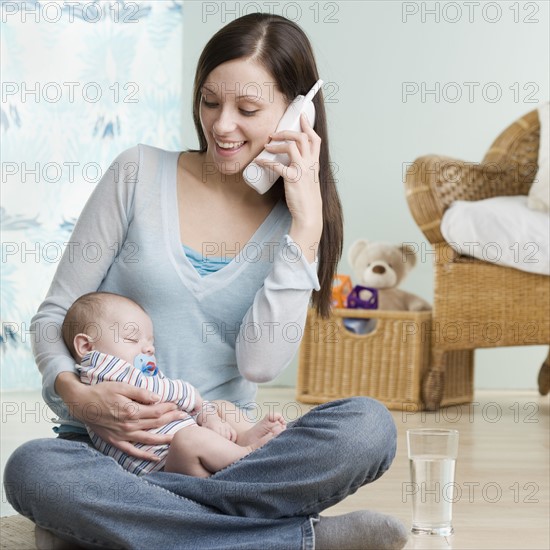 Mother on telephone with sleeping baby in her lap. Date : 2006