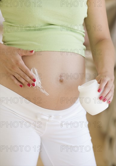 Pregnant woman applying lotion to belly. Date : 2007