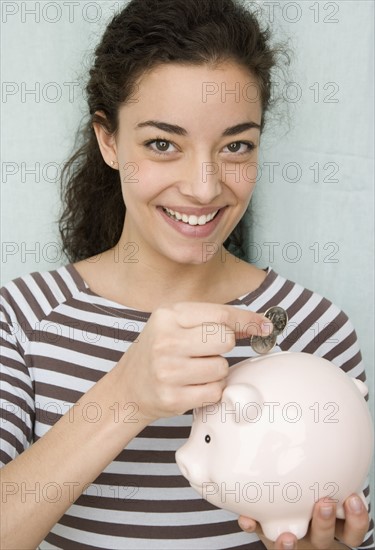 Woman putting coins in piggy bank. Date : 2007
