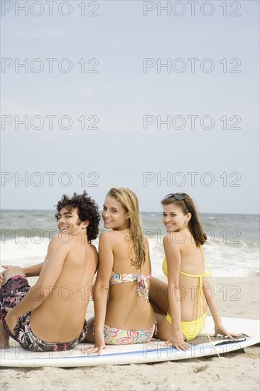 Friends sitting on surfboard at beach. Date : 2007