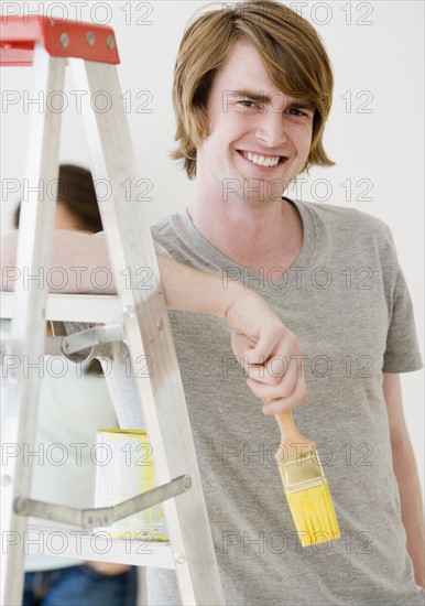 Man holding paintbrush next to ladder. Date : 2007