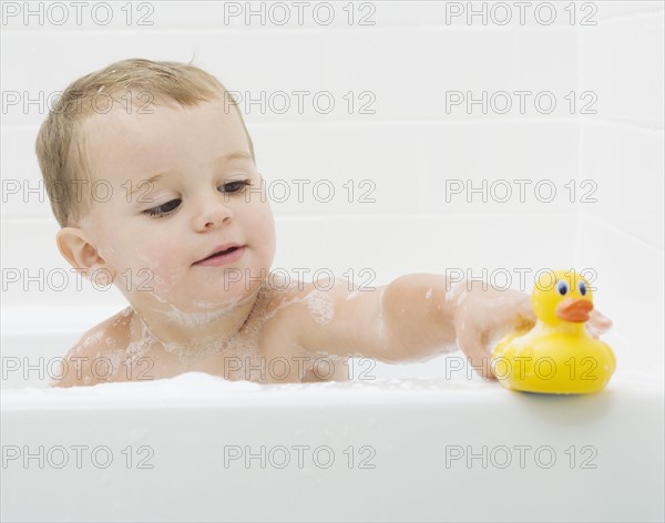 Baby playing with rubber duck in bath. Date : 2007