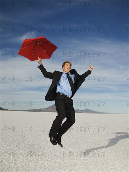 Businessman holding umbrella and jumping, Salt Flats, Utah, United States. Date : 2007