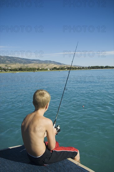 Boy fishing off dock in lake, Utah, United States. Date : 2007