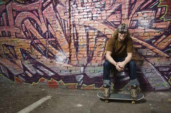 Young man with skateboard in front of graffitied wall. Date : 2007