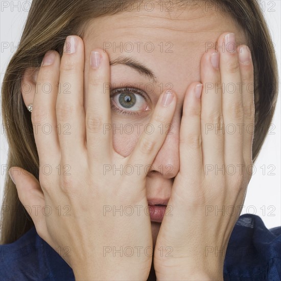 Woman peering through fingers.