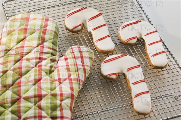 Candy cane cookies and oven mitt on cooling rack.